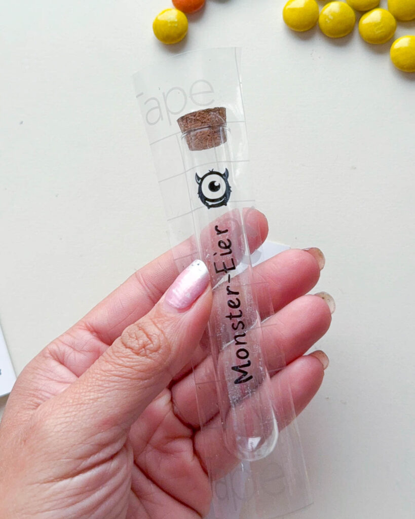 Halloween-Süßigkeiten im Reagenzglas: Plotter-Freebie mit M&Ms 7 Klebe anschließend Übertragungsfolie über den Schriftzug und streiche sie mit einem Rakel fest. Ziehe das Trägerpapier vorsichtig ab, sodass das Motiv an der Übertragungsfolie haftet.
